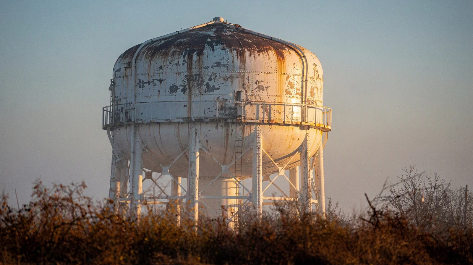 Painted municipal water tower rising above autumn haze, house numbers faded on the steel tank