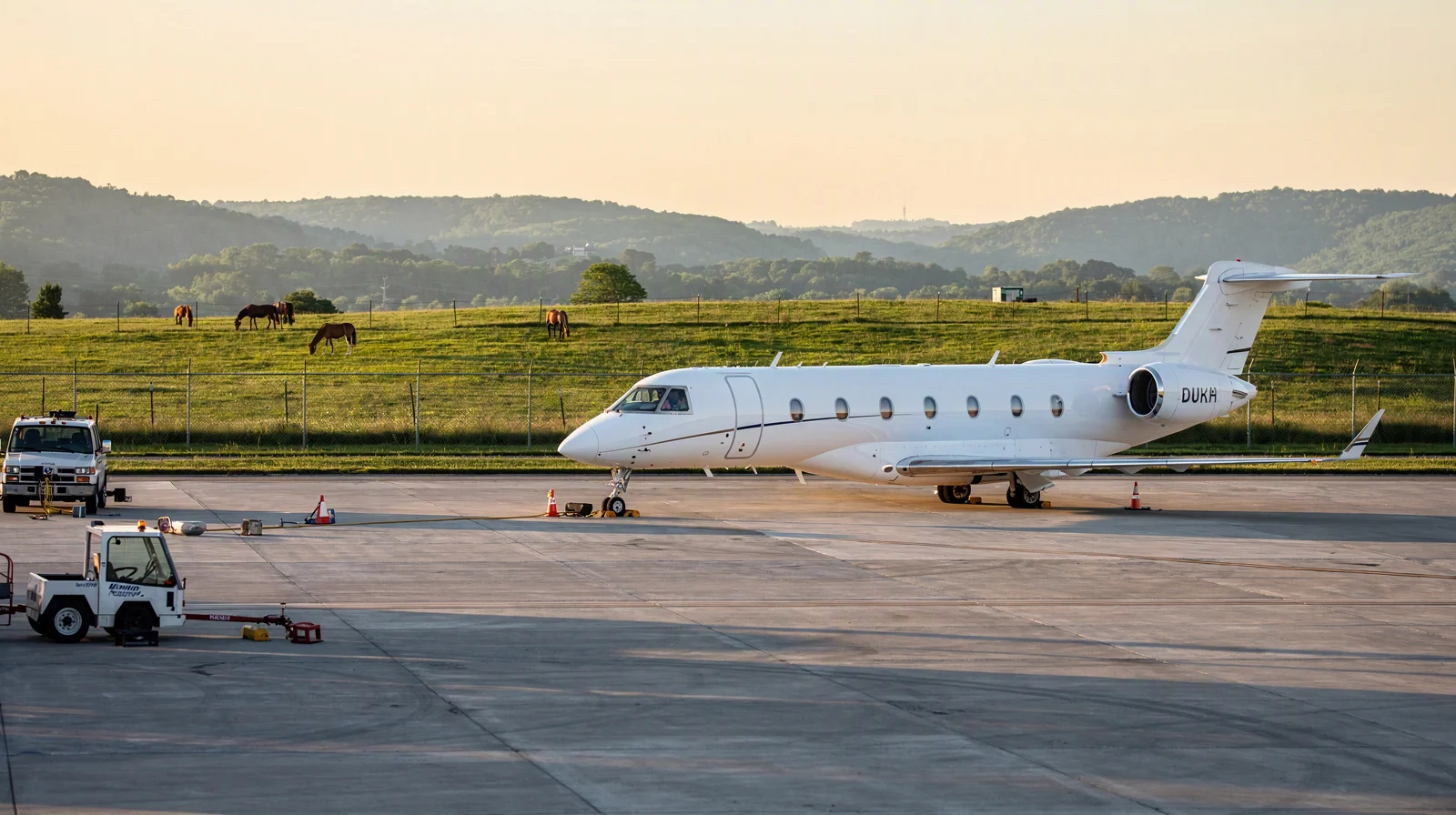 Business jet on the general aviation ramp at dawn with bluegrass pasture beyond the perimeter fence