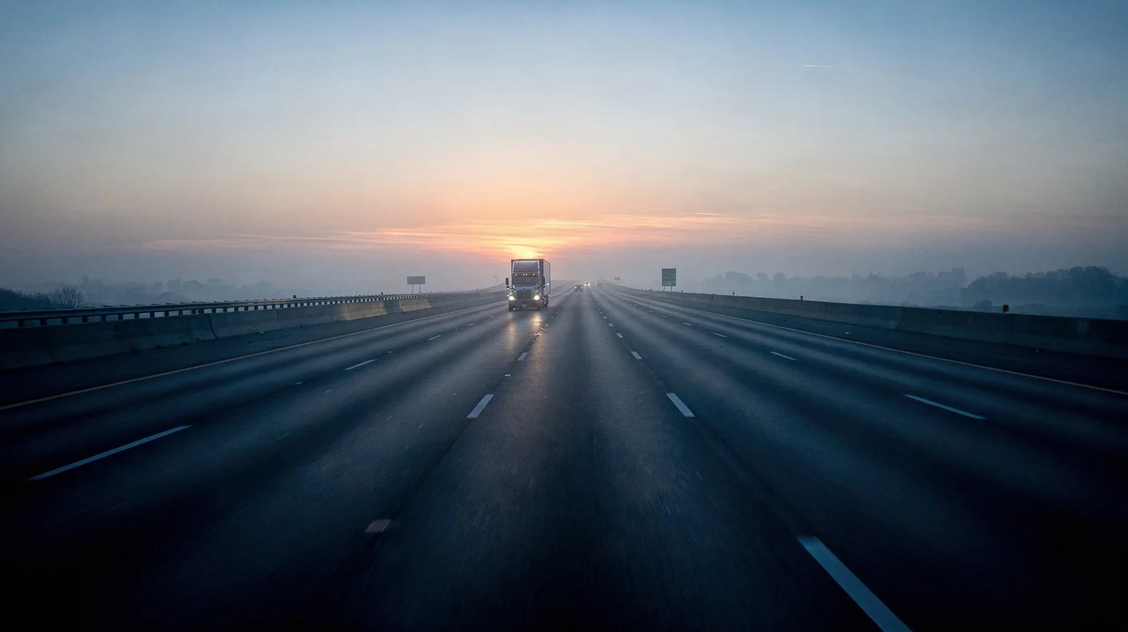 Empty interstate at first light with one distant semi truck and heat haze, no readable signage
