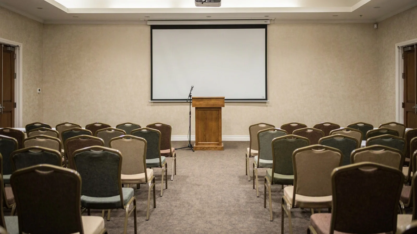 Rows of empty chairs facing a wooden auction lectern and blank projection screen in a neutral sale room, soft overhead light