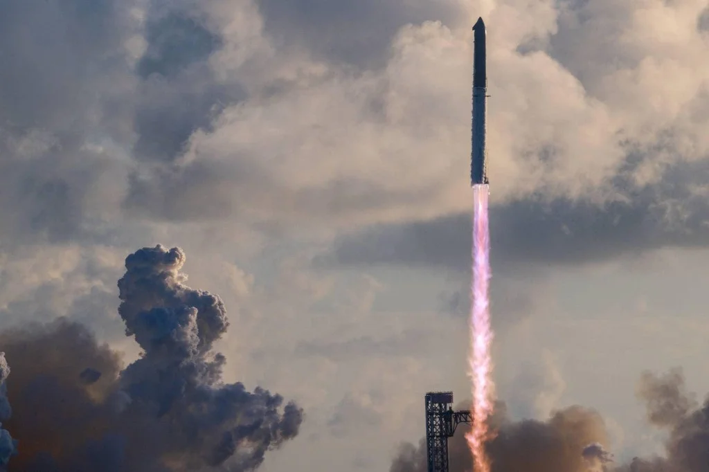 A super-heavy launch vehicle climbs through sunset-lit clouds, a long violet-orange exhaust trail streaming toward the pad below