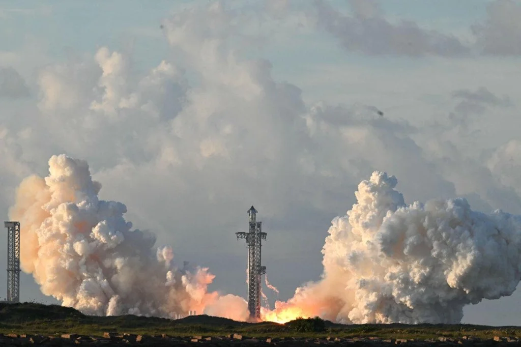 Starship at ignition on the pad, twin plumes of steam and exhaust erupting symmetrically around the launch tower